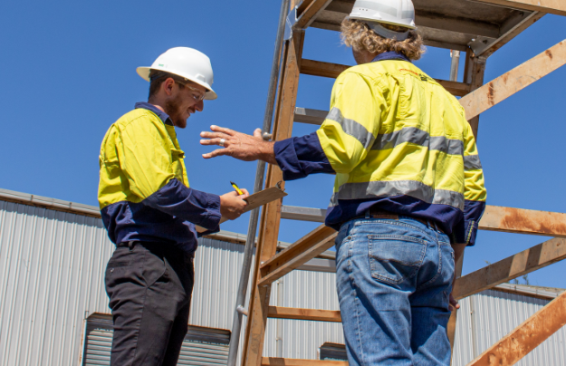 two men talking with one taking notes next to a ladder