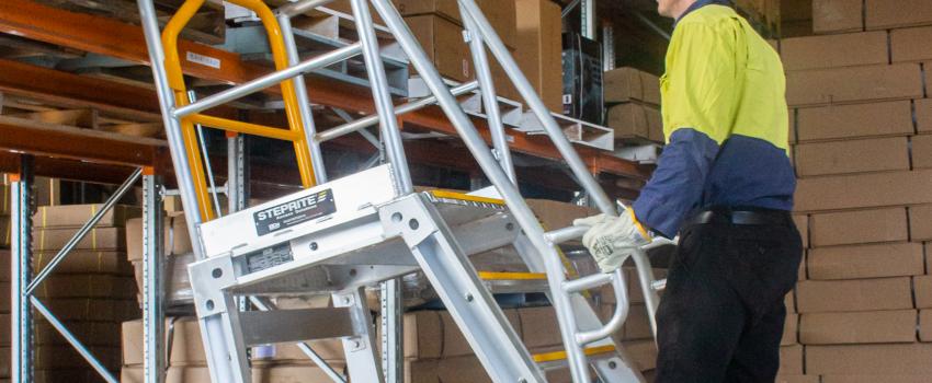 man rolling access ladder up to shelving