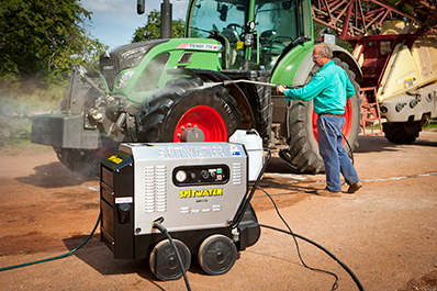 Man pressure washing agricultural equipment behind spitwater pressure cleaner
