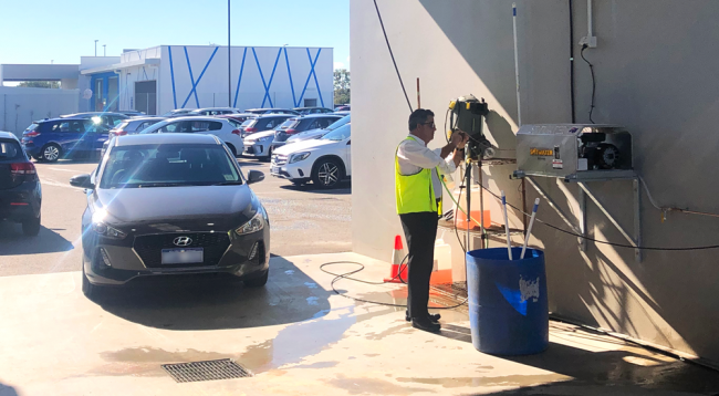 Man working on wall mounted pressure cleaner in a wash bay with a car coming in